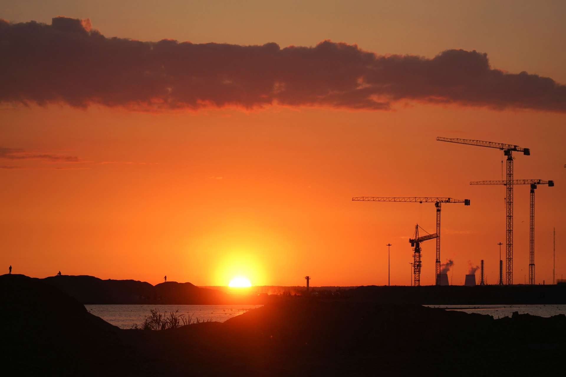 Coucher de soleil sur un chantier d'infrastructure avec silhouettes de grues