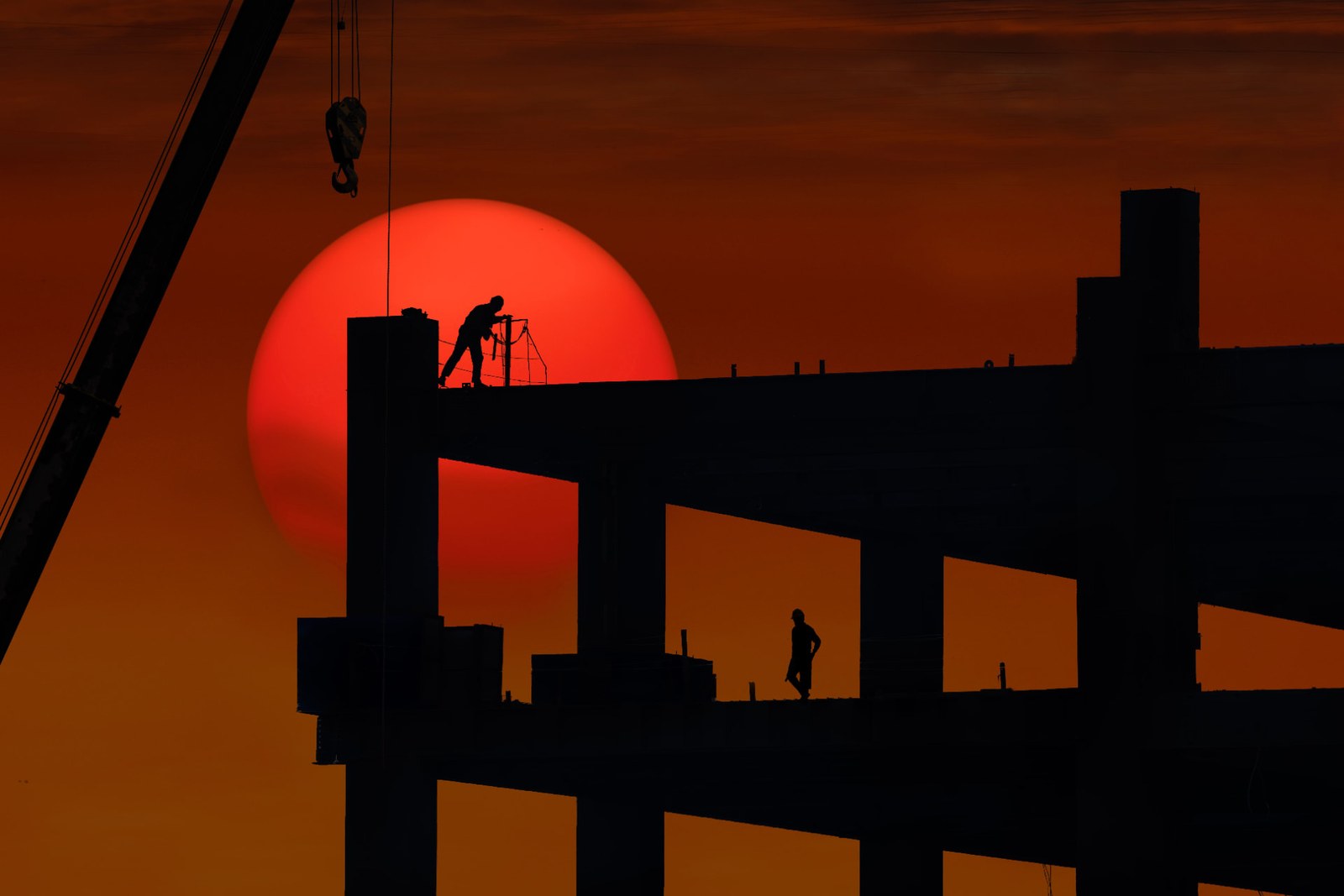 Silhouettes d'ouvriers et de grue sur une structure en construction au coucher du soleil